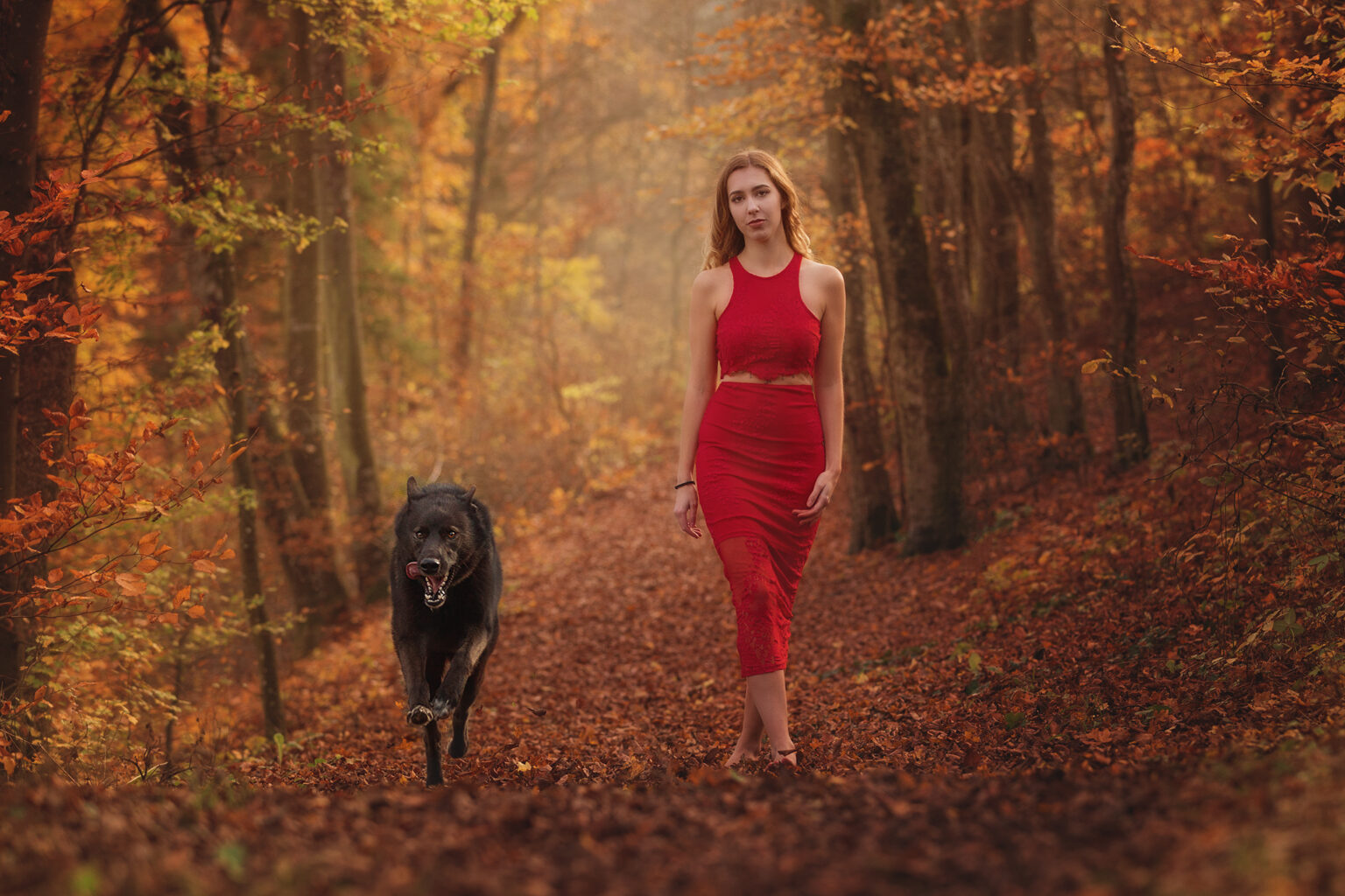 Frau im roten Kleid geht mit ihrem Hund durch den Herbstwald