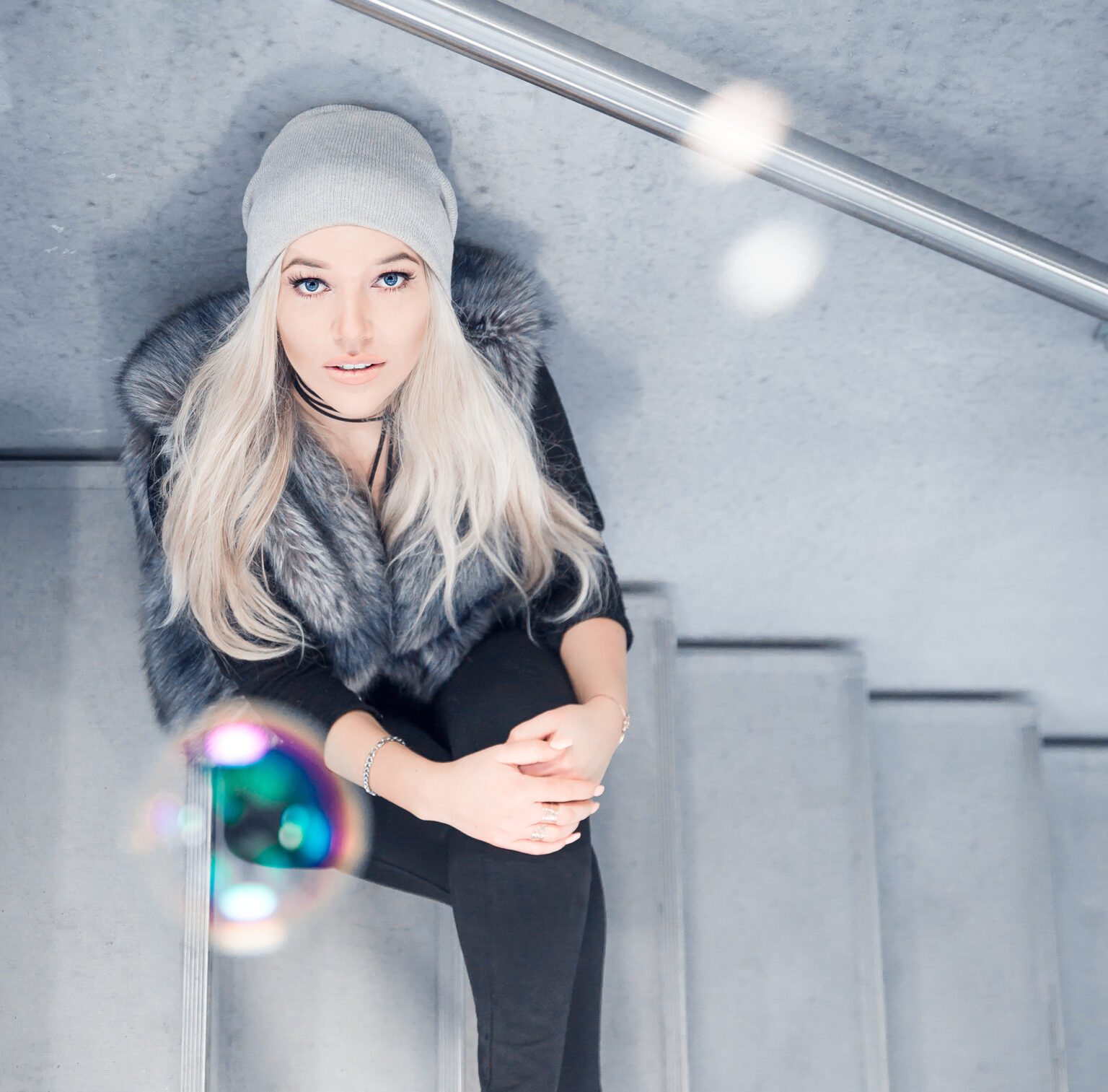 Junge Frau mit Mütze auf einer Betontreppe, von oben fotografiert